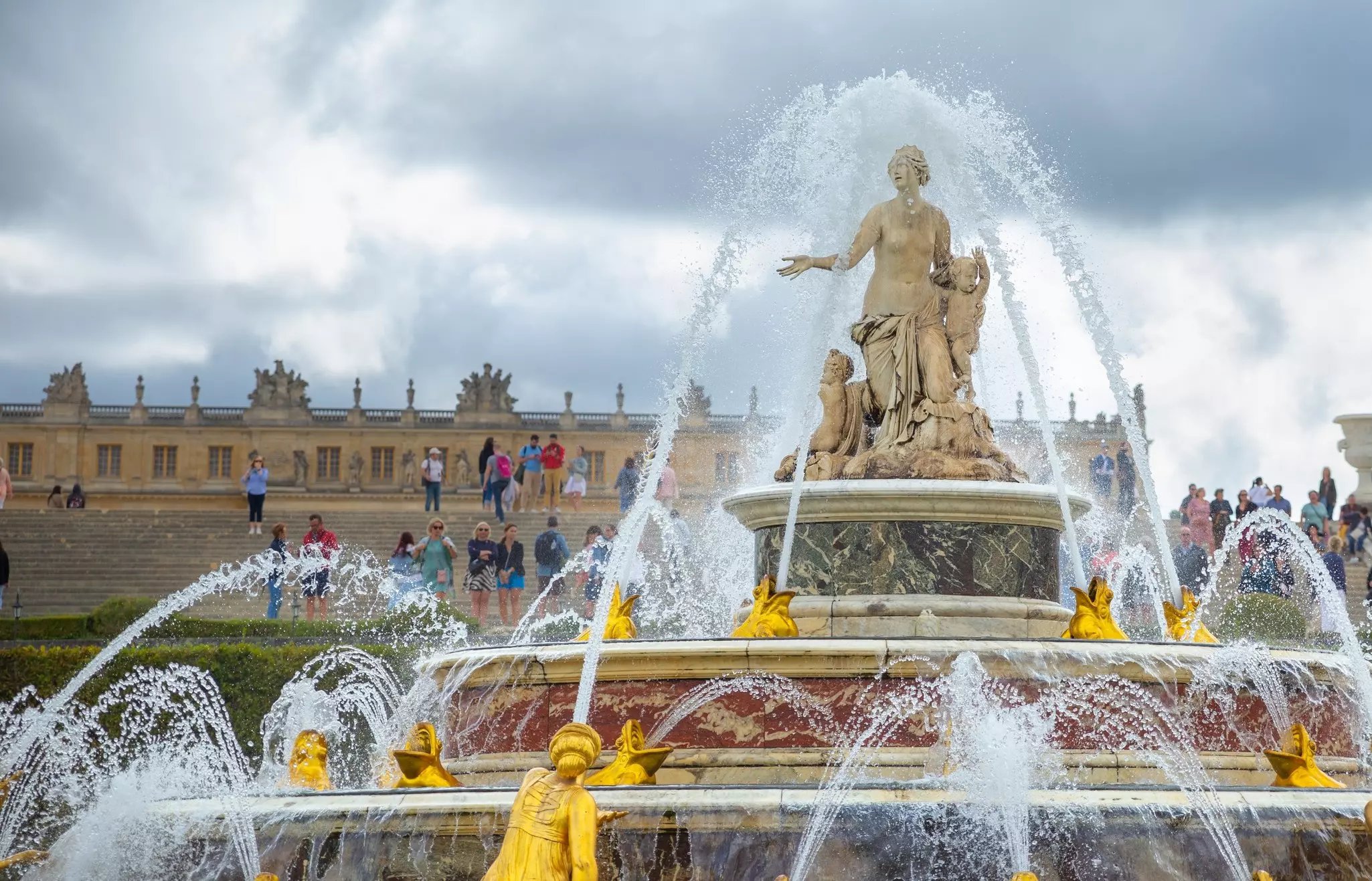 A fountain spurts water; a classical sculpture is at the top, with smaller gold sculptures around the perimeter.