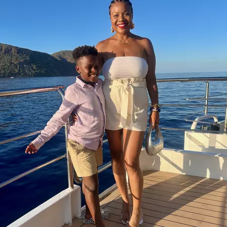 A woman and child stand by a railing on a boat with the sea behind them.