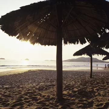 Mexico, Ixtapa, ocean sunset with couples walking along shoreline, umbrellas in sand.