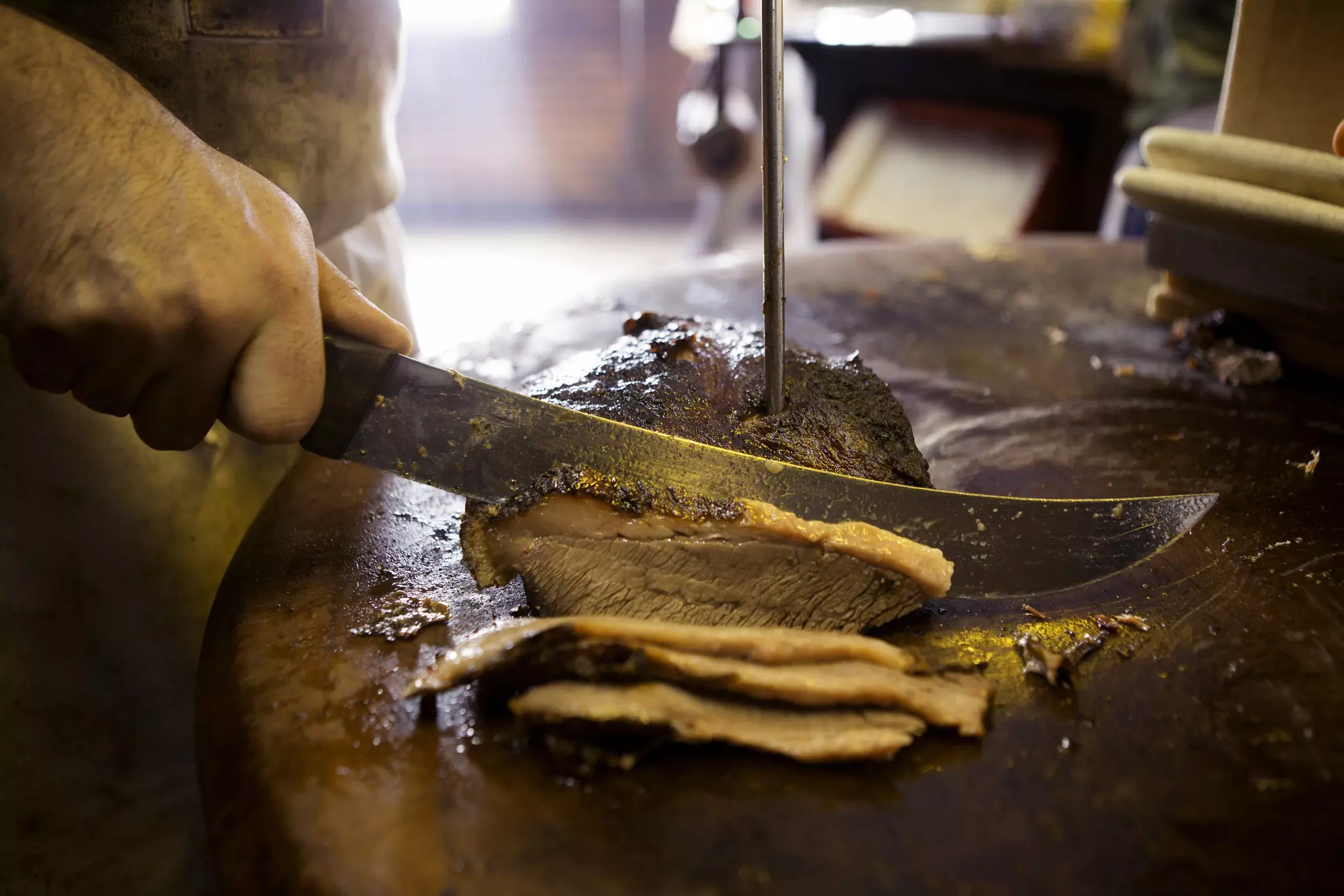 A worker slices barbecue meat for a customer in a restaurant.