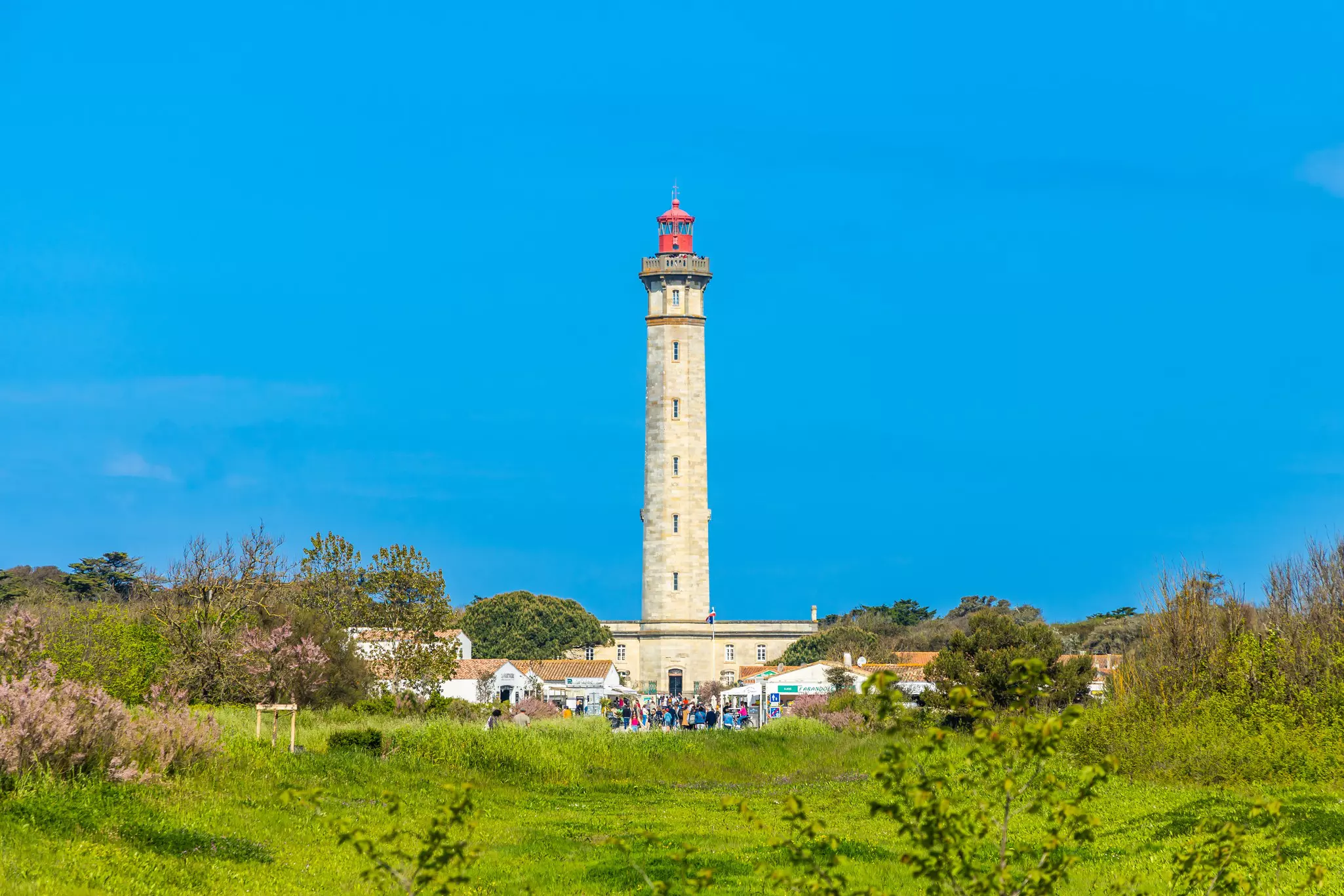 The tall stone tower of a lighthouse against a blue sky.