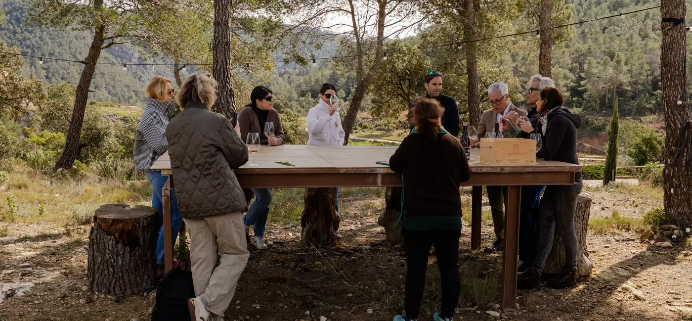 People outdoors stand around a large wooden table.