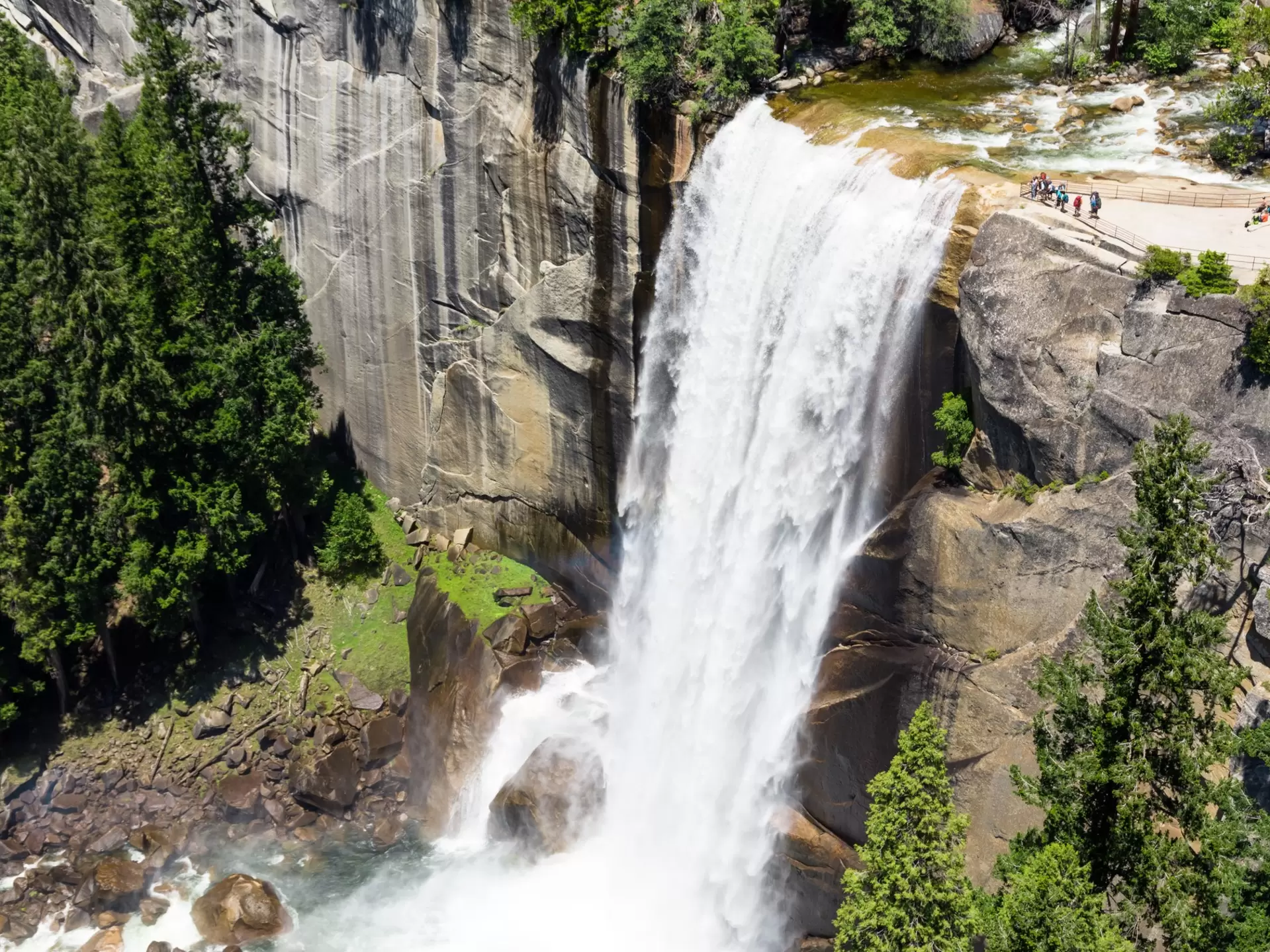 A waterfall in heavy flow cascades down into a pool. People watch from a viewing platform
