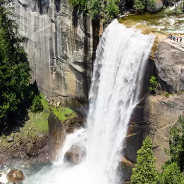 A waterfall in heavy flow cascades down into a pool. People watch from a viewing platform