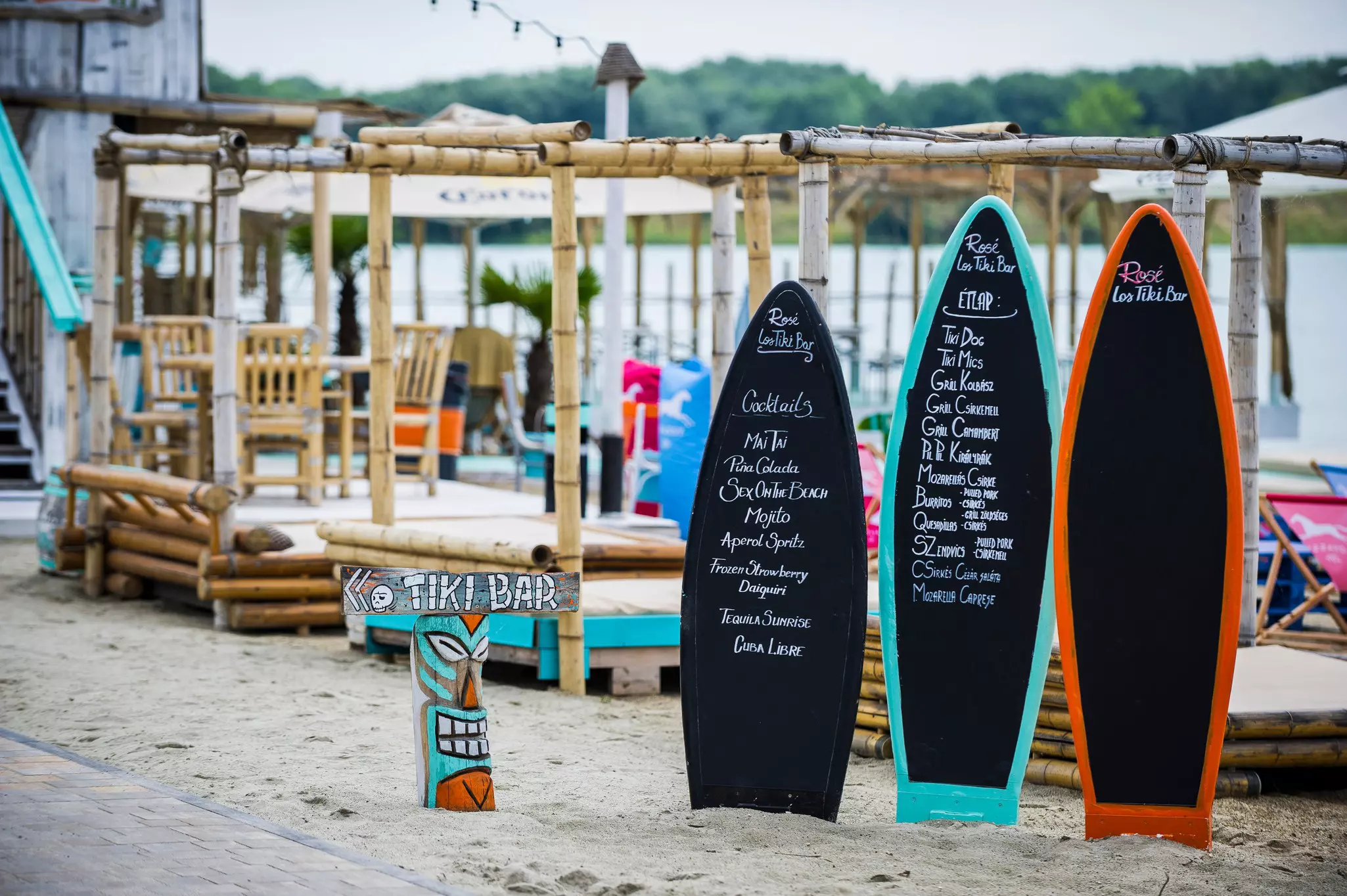 Surfboards are printed with menu items and information at a beach lined with four-poster cabanas
