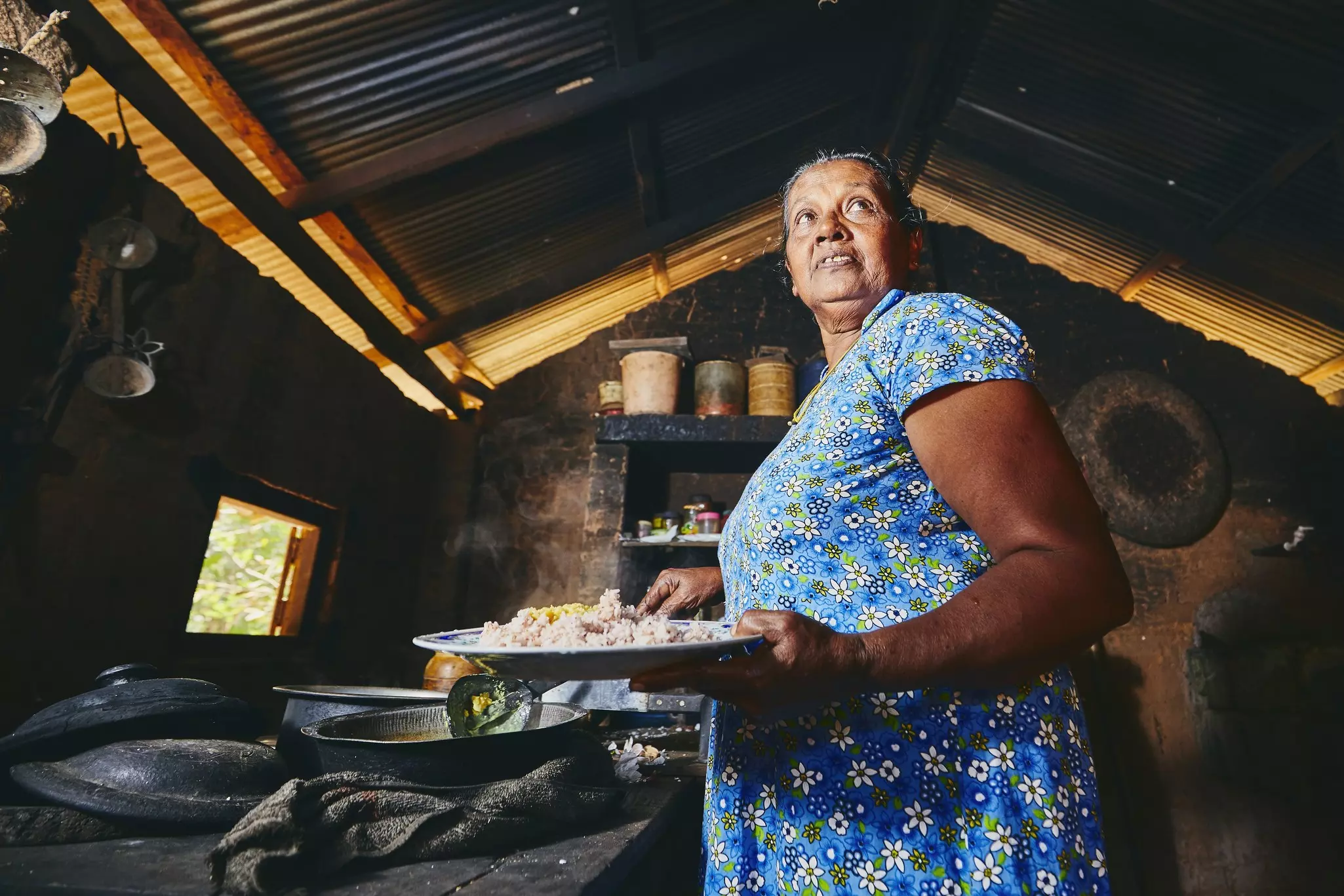 A woman wearing a blue dress prepares a meal with rice in a home kitchen