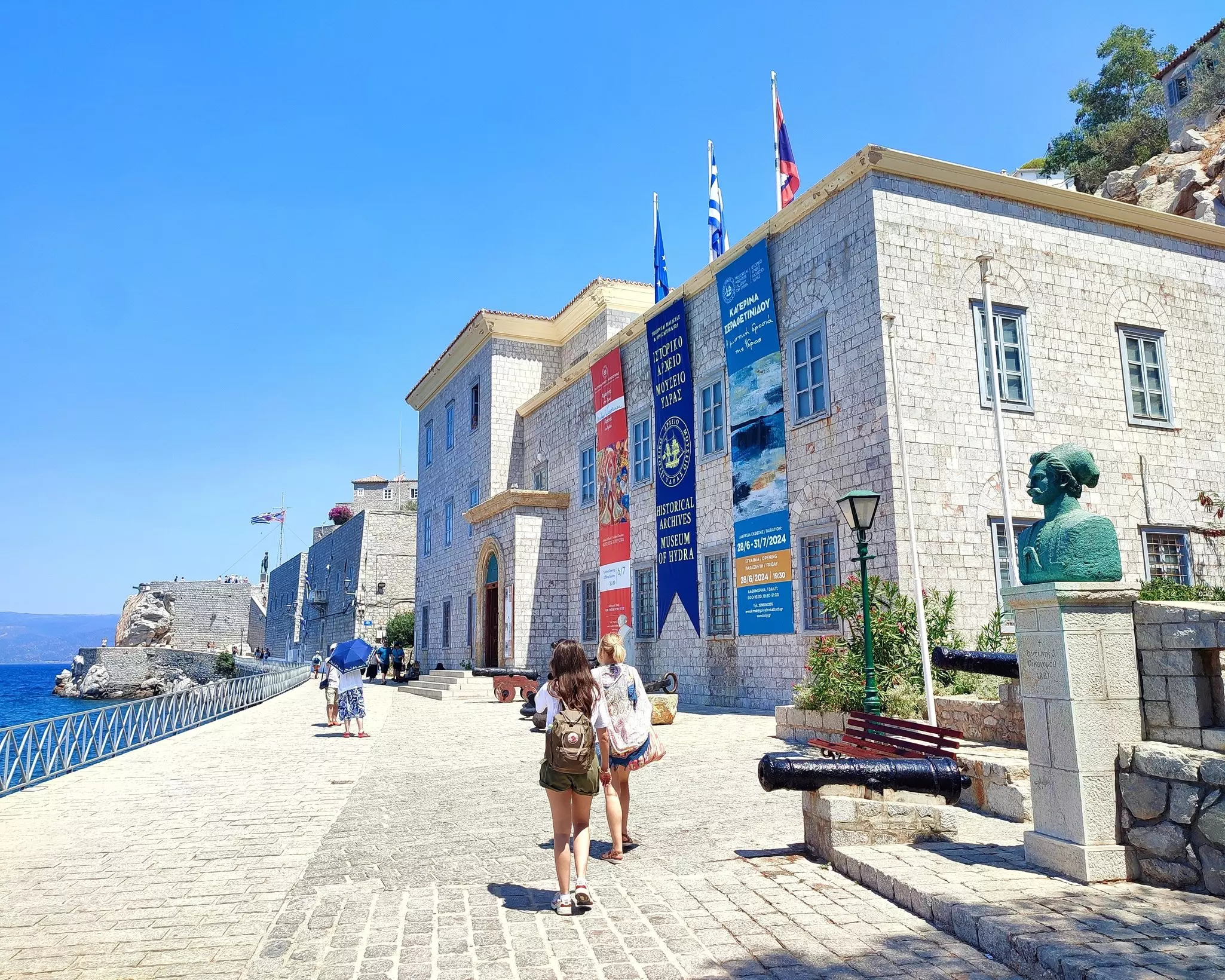 HYDRA, GREECE - JULY 31ST 2024: Exterior view of the Historical Archives Museum of Hydra, with the bust of 1821 naval captain Antonis Oikonomou visible on the right and Kavos Castle in the distance., License Type: media, Download Time: 2025-09-22T19:40:35.000Z, User: bhealy950, Editorial: true, purchase_order: 65050 - Digital Destinations and Articles, job: Lonely Planet Online Editorial, client: Best things to do in Hydra, other: Brian Healy