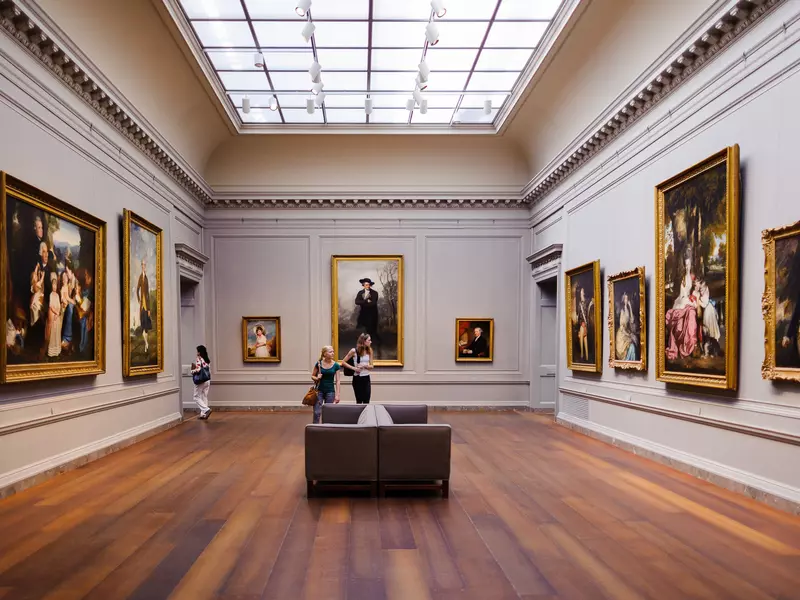 Interior of the National Gallery of Art, a national art museum in Washington, D.C. The walls are covered with giant paintings as visitors walk around the room