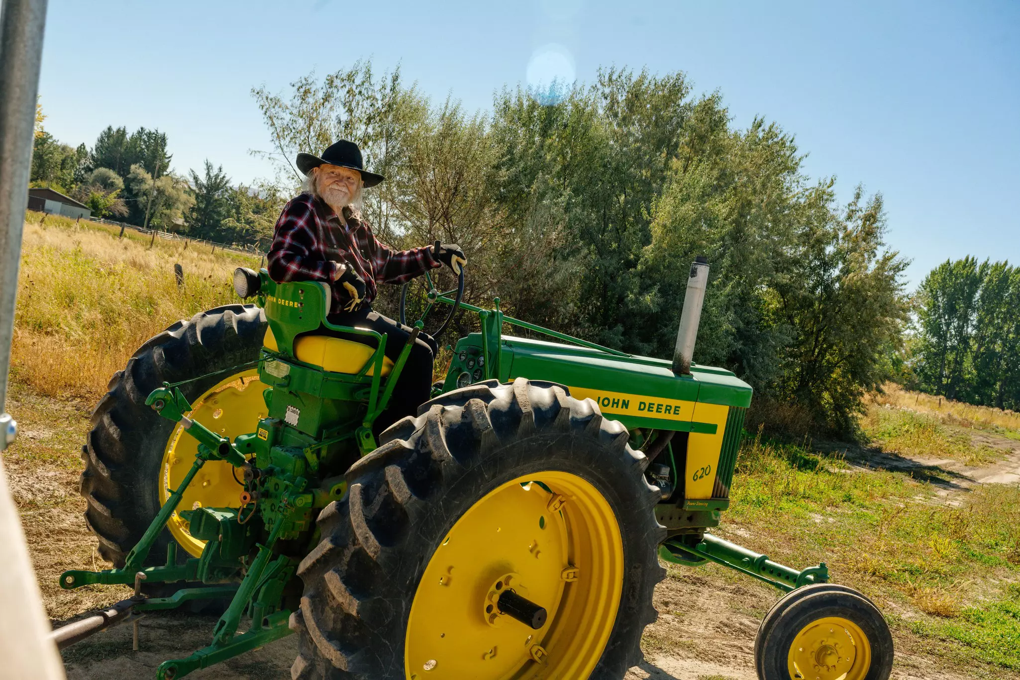 Bearded man in a black cowboy hat on a yellow and green tractor out in a field