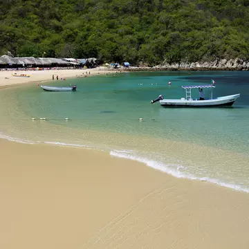 Two boats in shallow turquoise water by a sandy beach in Mexico.