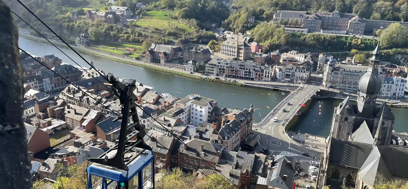 A cable car travels up a steep incline. A river below winds through a city with the distinct onion-dome of a church and colorful buildings below.