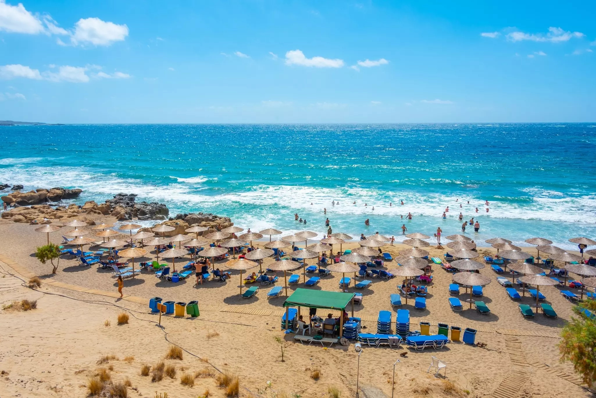A sunny beach lined with parasols, sunbeds and a view of people swimming in the water.