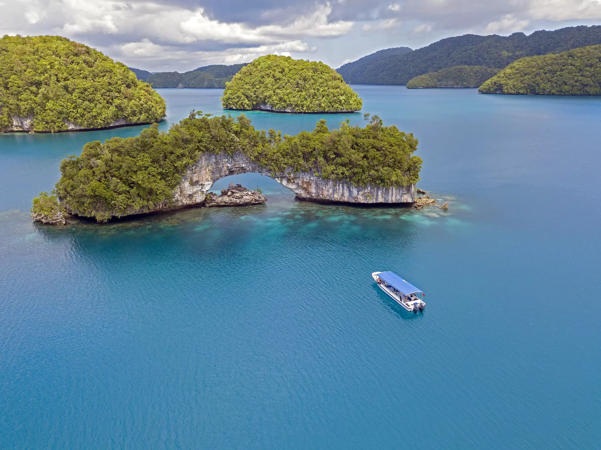 A small boat travels through dark blue ocean towards an island with a large rock arch.