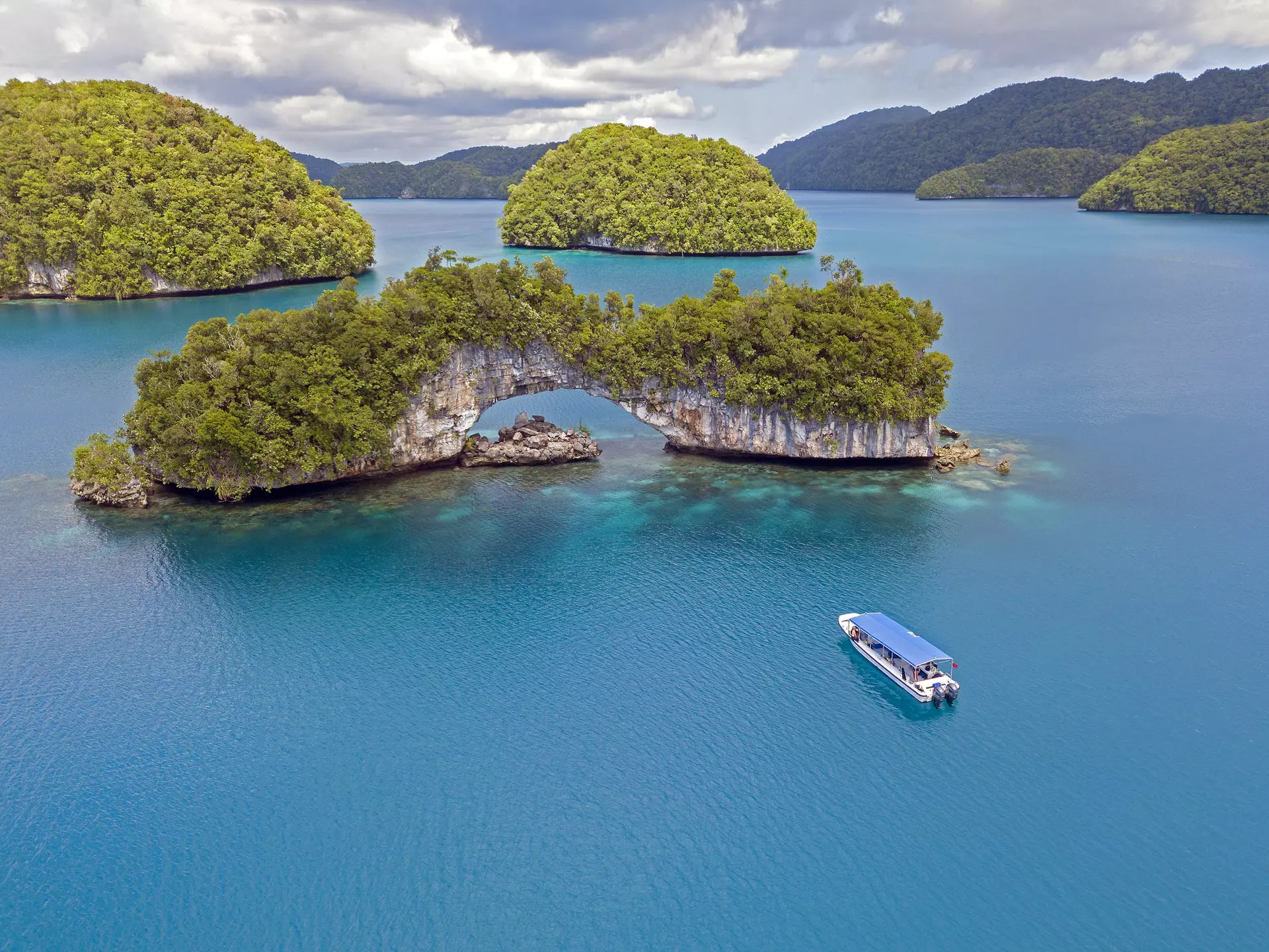 A small boat travels through dark blue ocean towards an island with a large rock arch.