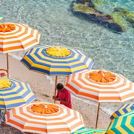 A man adjusts a striped umbrella on a beach.