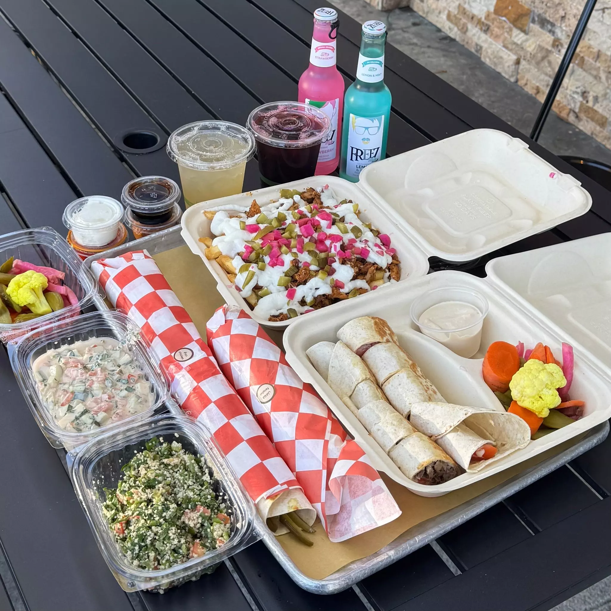 A picnic table laid out with wraps, salads, pickled vegetables, dips and soft drinks.