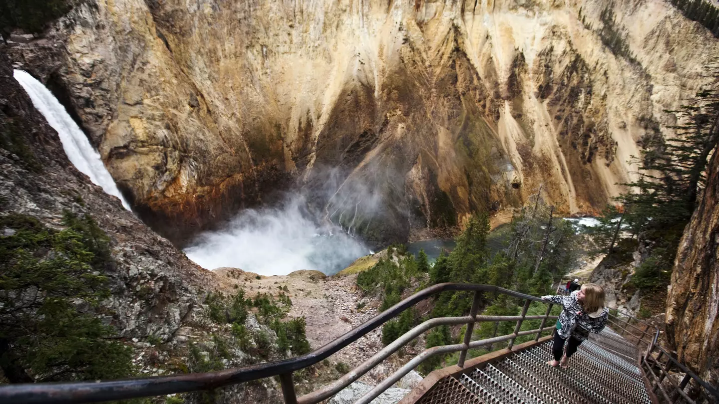 A young woman walks up a narrow staircase, winding down to an overlook of Yellowstone Falls