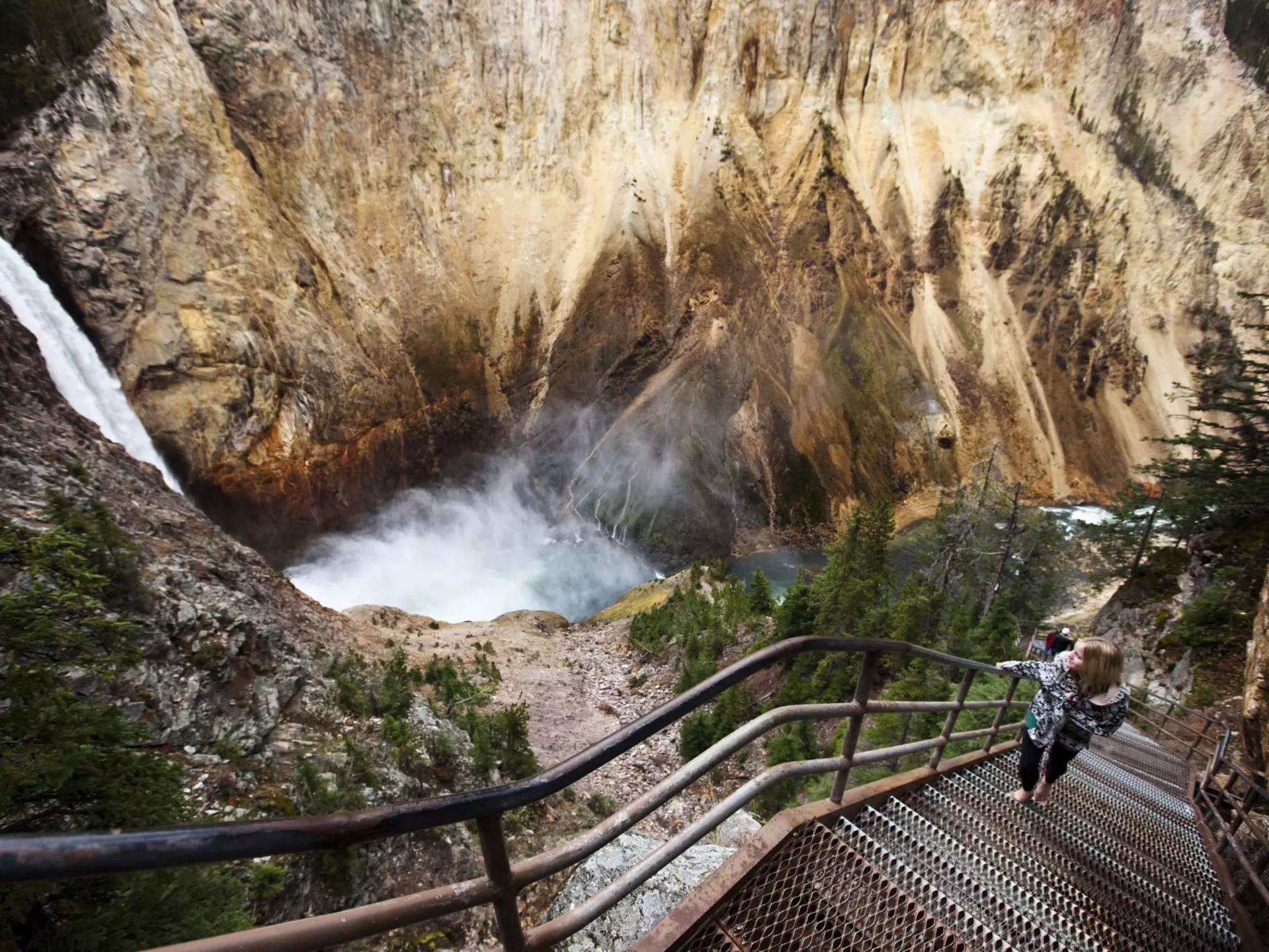A young woman walks up a narrow staircase, winding down to an overlook of Yellowstone Falls