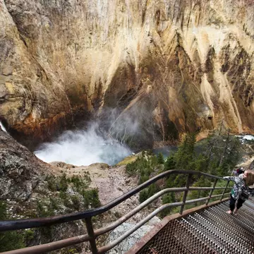 A young woman walks up a narrow staircase, winding down to an overlook of Yellowstone Falls