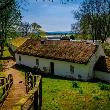 Whitewashed thatched-roof cottage with a green lawn at a rural heritage farm