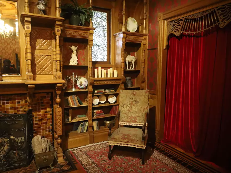 A room with heavy drapes, wooden shelves and old-fashioned decor.