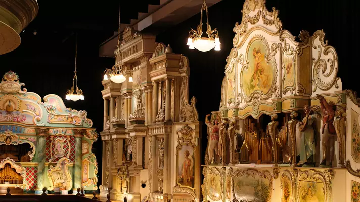 Ornate organs and musical instruments on display in a dark museum room.
