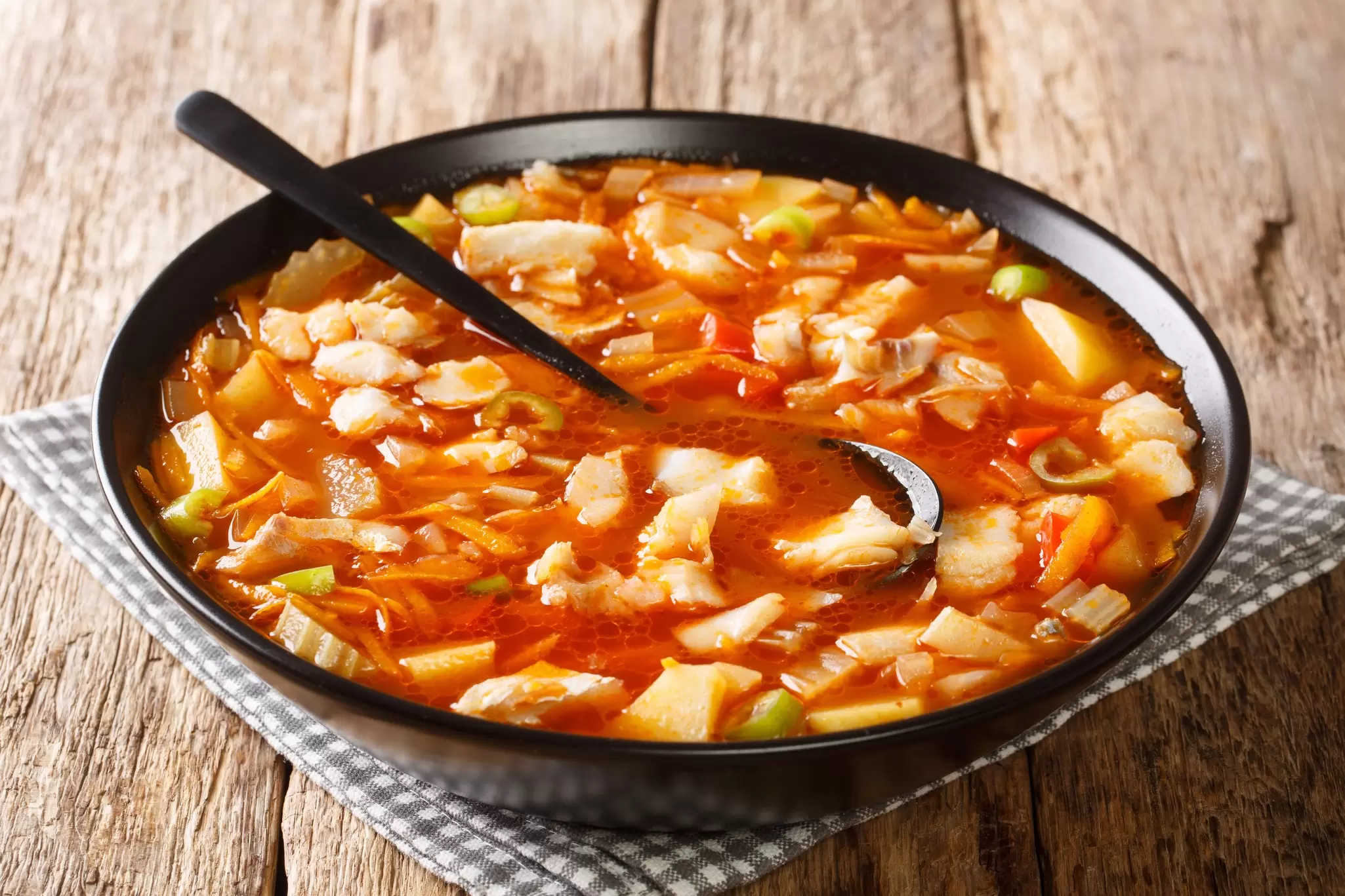 A black bowl filled with a fish chowder in an orange-colored broth