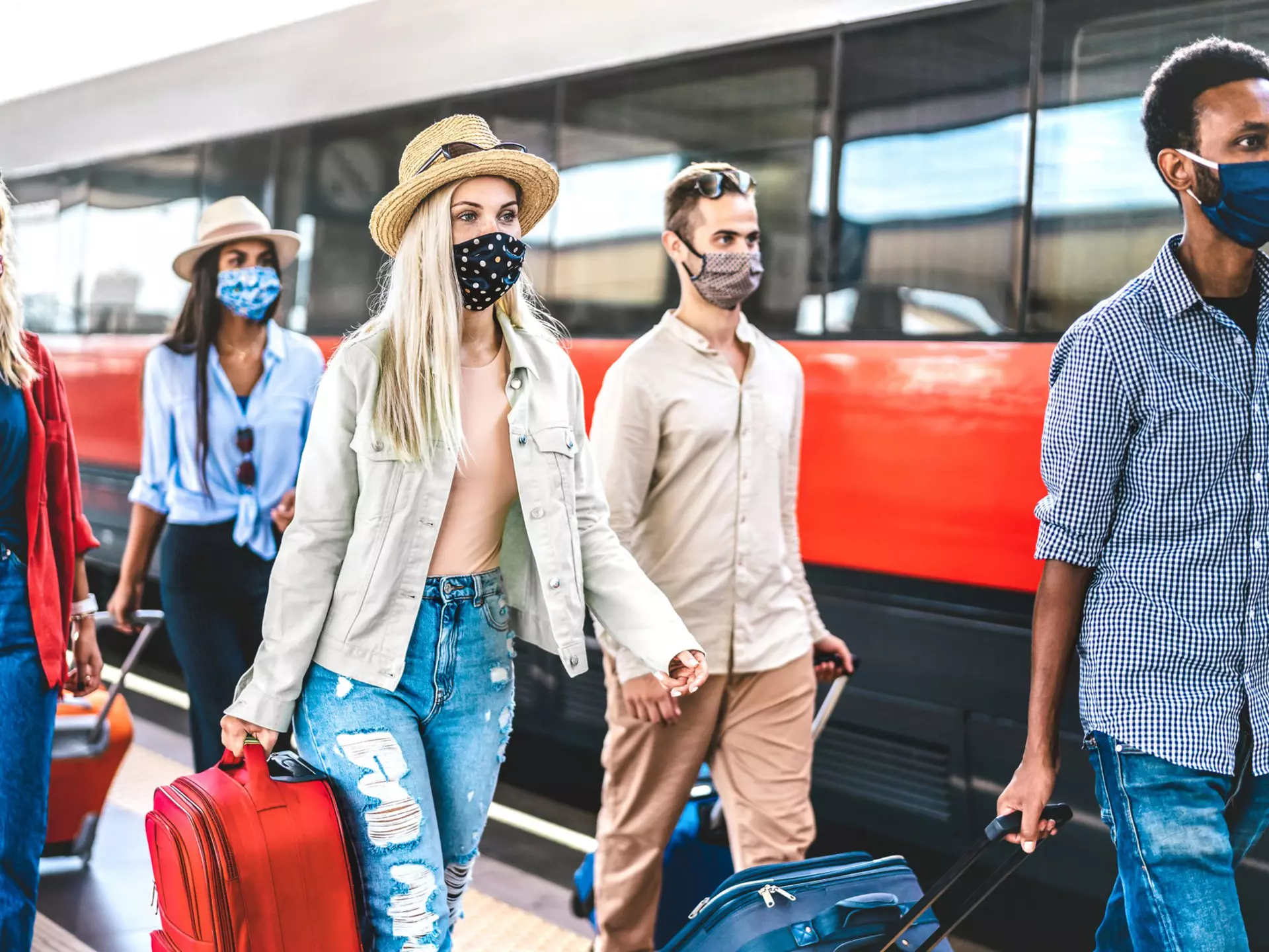 Multiracial friends group walking at railway station platform - New normal travel concept with young travelers on social distancing and face covered by protective mask - Focus on blonde girl with hat