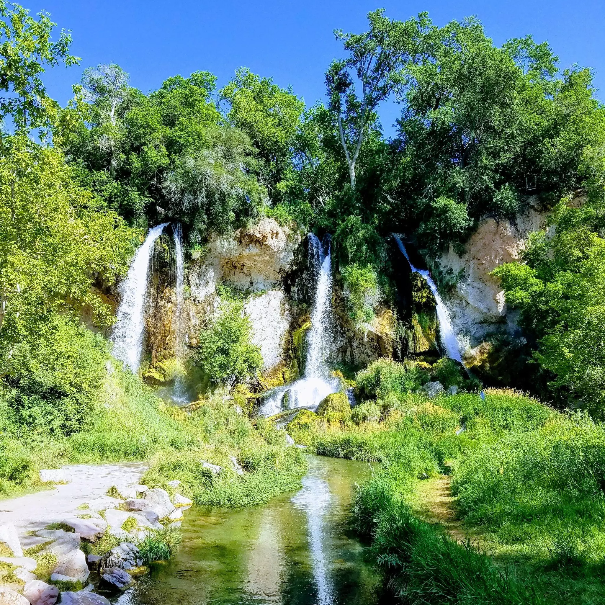 Three separate falls, surrounded in green foliage, plunge off a cliff and into the same river.