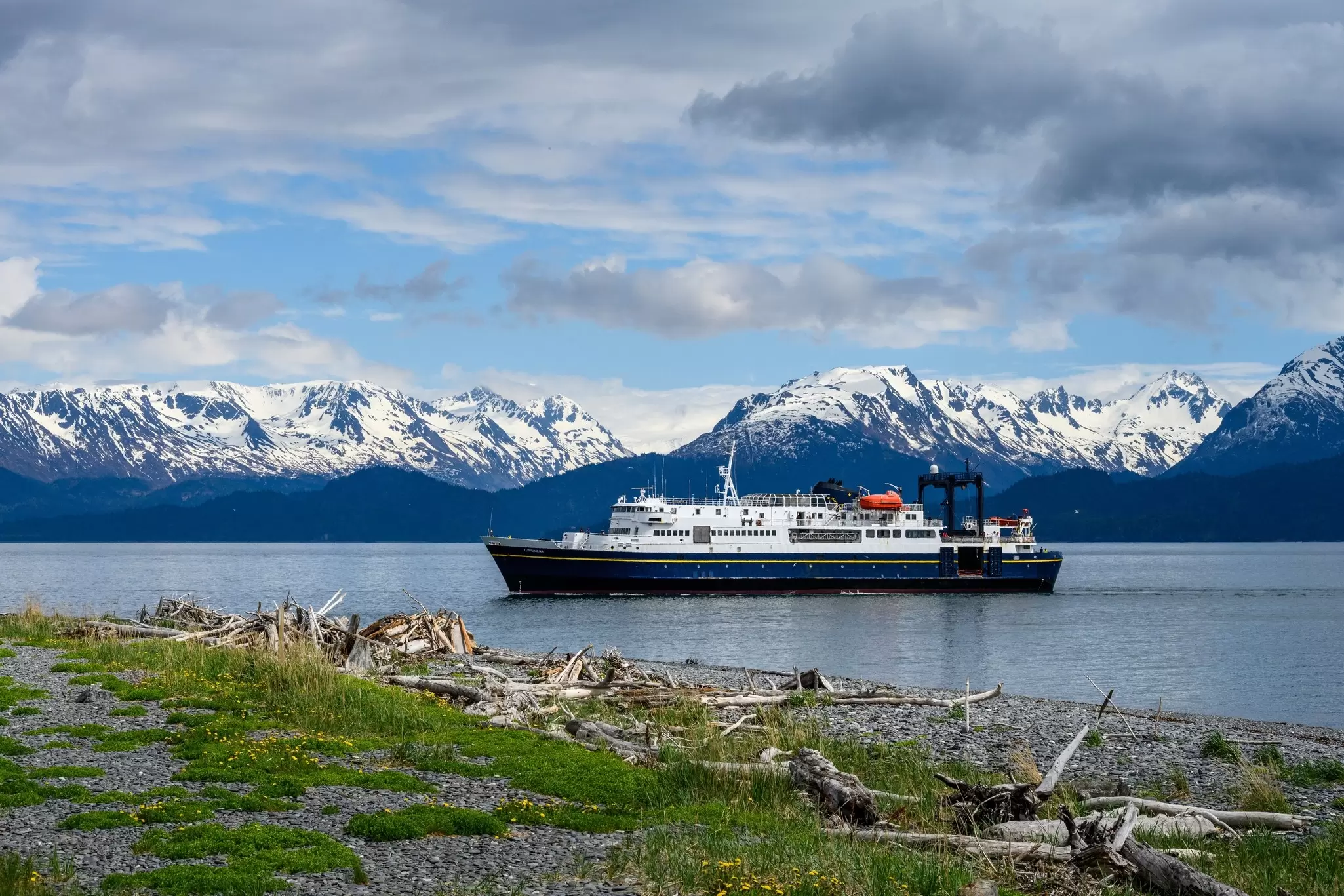 A passenger ferry on the Alaska Marine Highway sailing past snow-capped mountains.