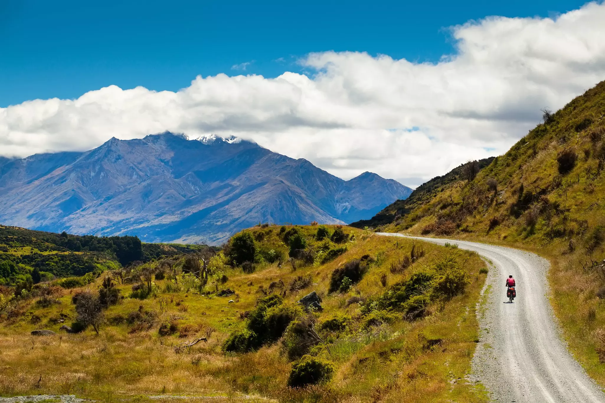 A mountain biker rides along a winding gravel track in a mountain valley.