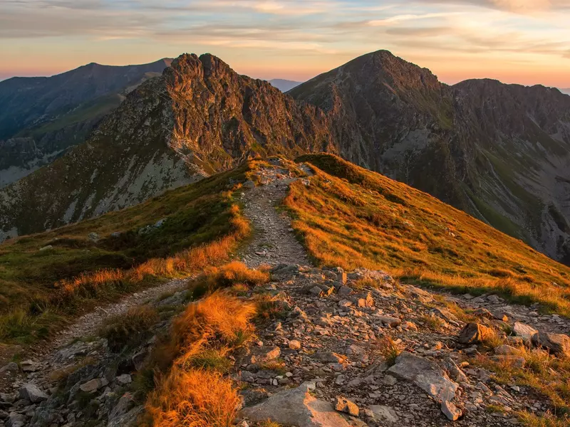 A trail on a mountain ridge, with autumn grass and a colorful sky.