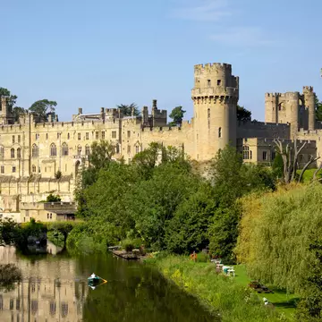 Medieval castle towers and battlements rising above a river and trees.