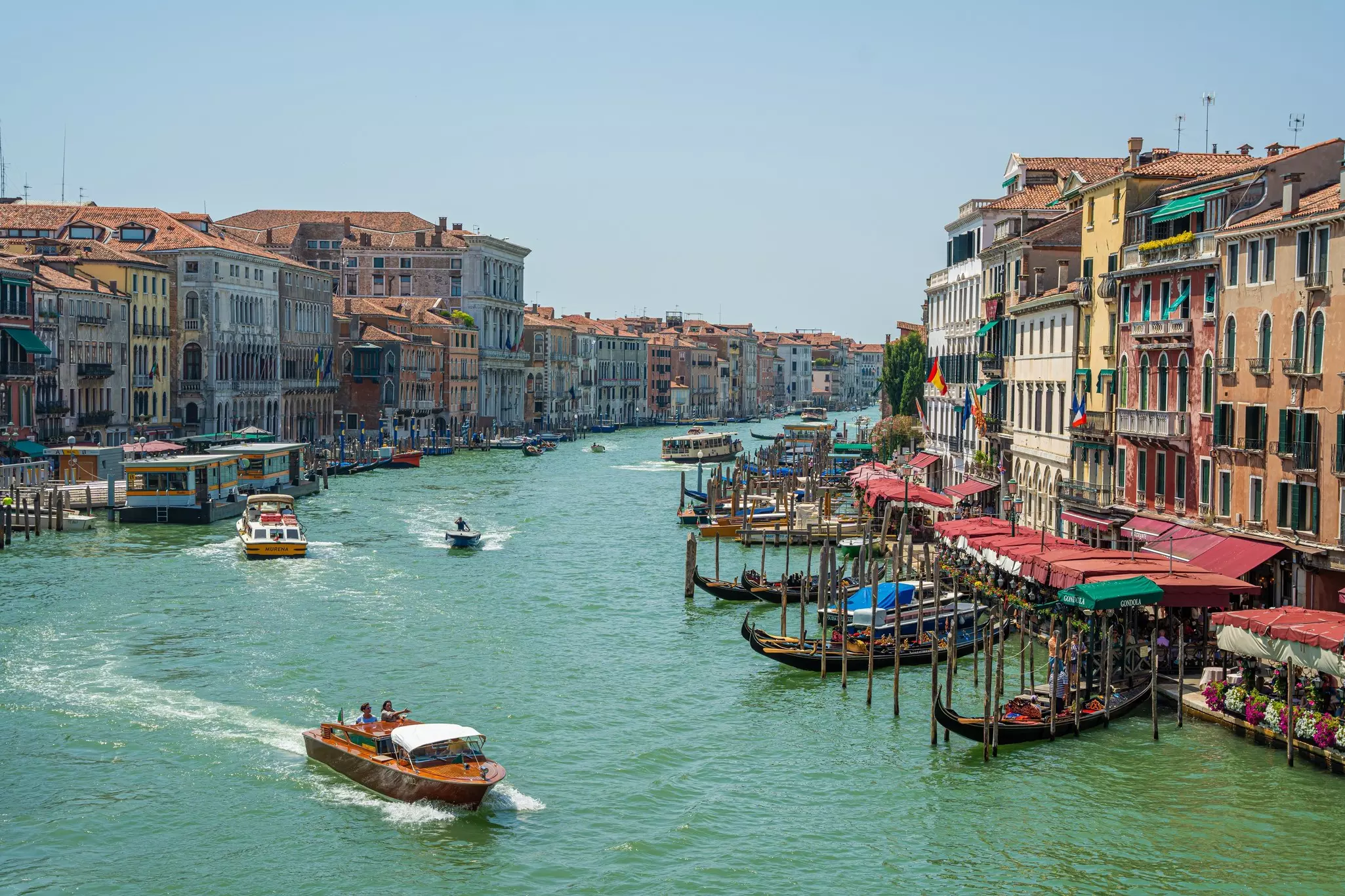 Boats in a turquoise canal with buildings lining the shoreline.
