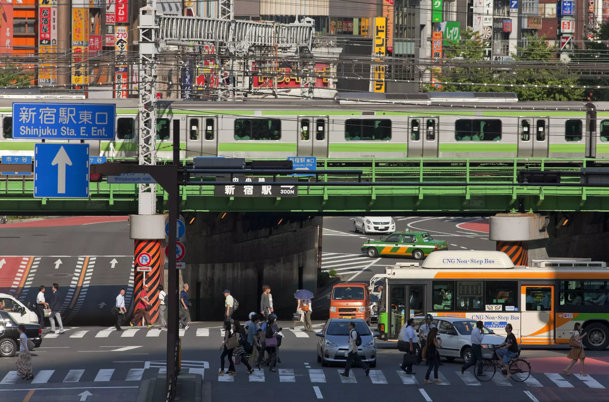The Yamonte Line, in Tokyo Japan, on a sunny day. Cars and pedestrians passing by are in view.