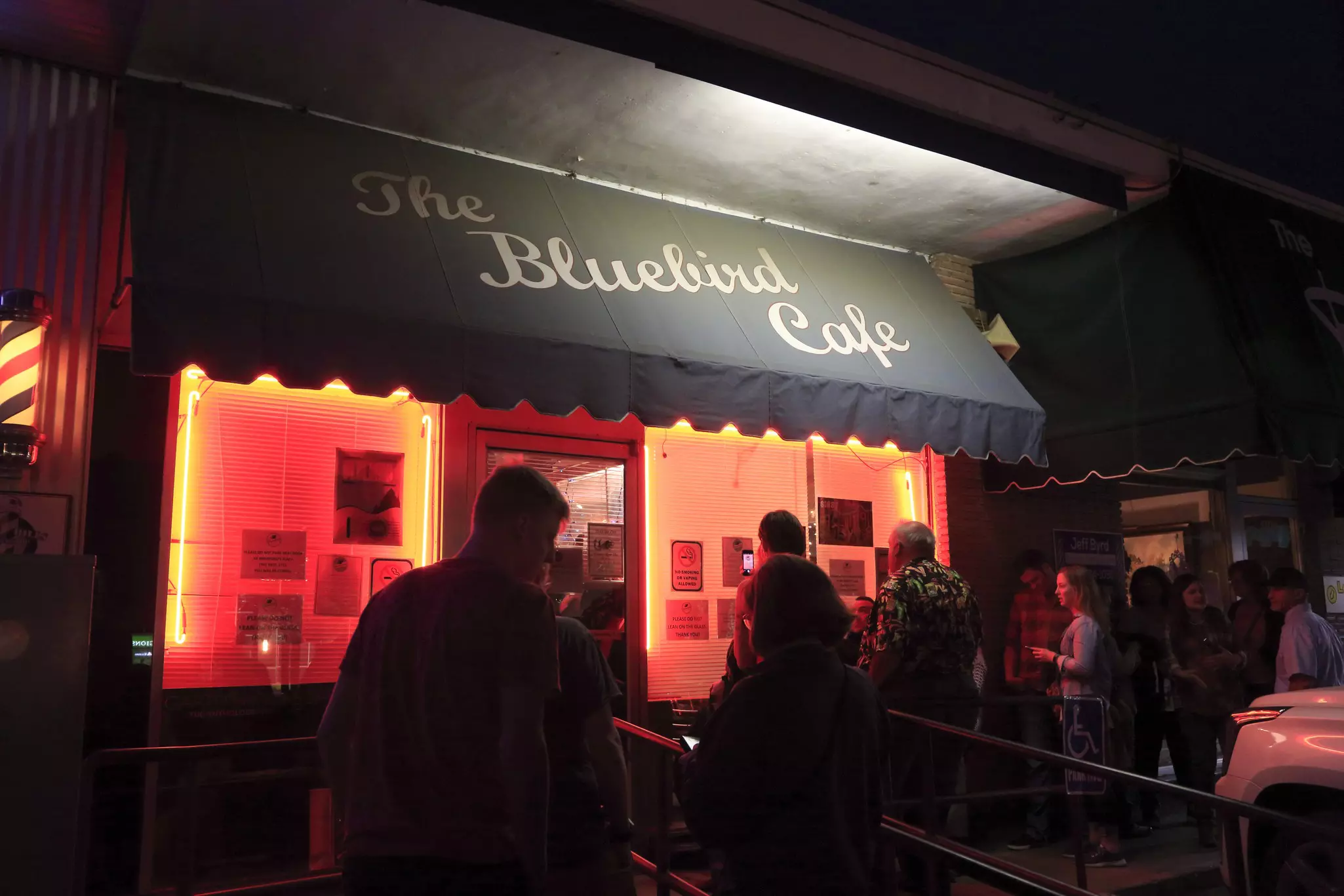 People waiting in line to get into a club at night. The awning over the entrance says "The Bluebird Cafe."