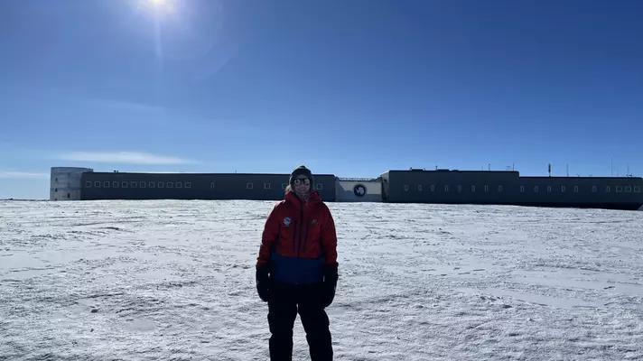 A woman stands in front of a low-rise long building on a snow-covered plateau