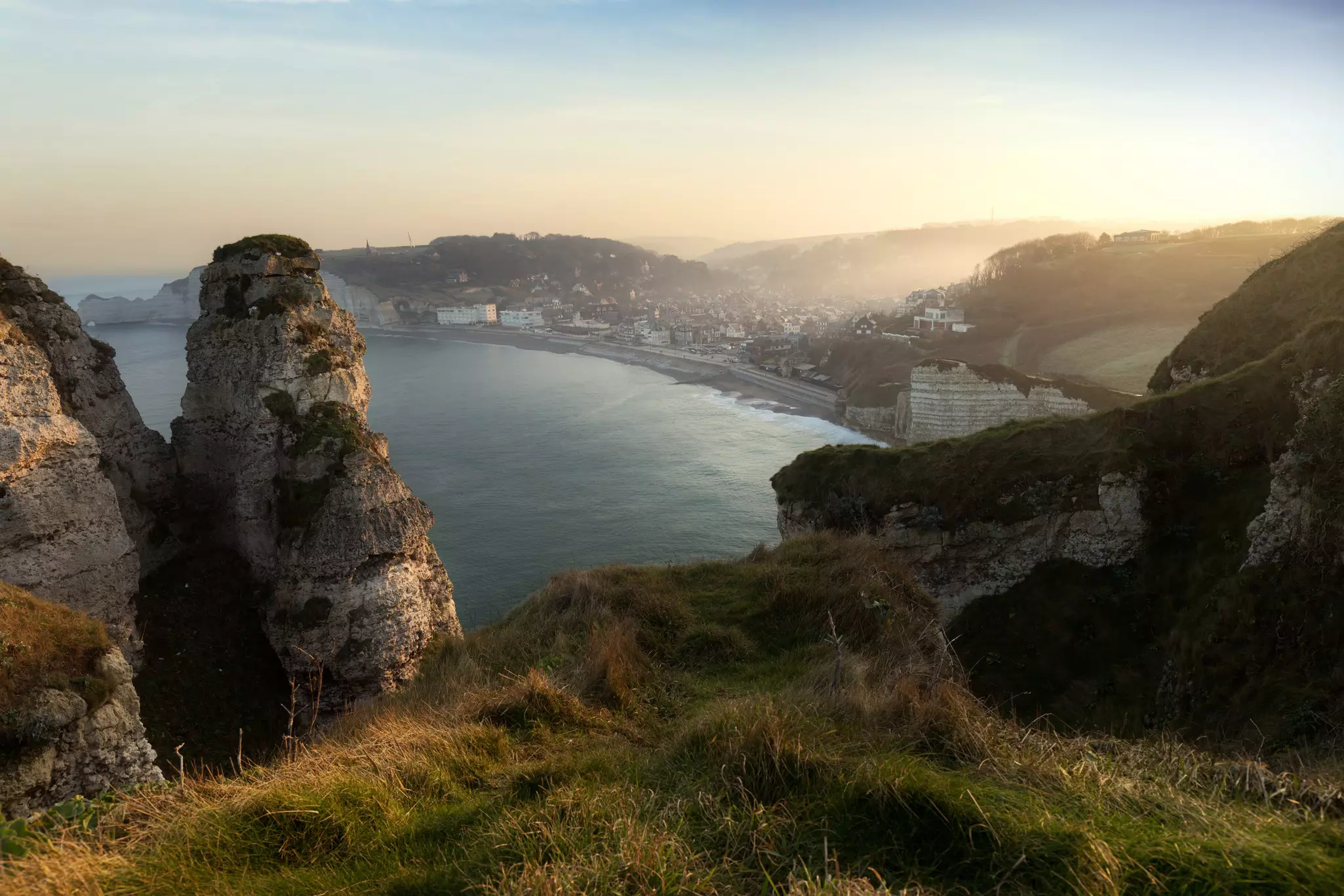 The sun rises over Étretat, as seen from the nearby cliffs overlooking the town.