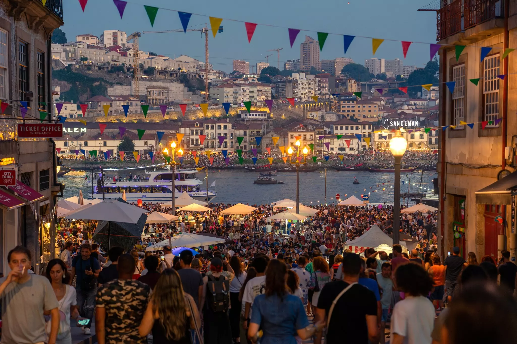 Revellers fill the streets during an evening festival beside a river.