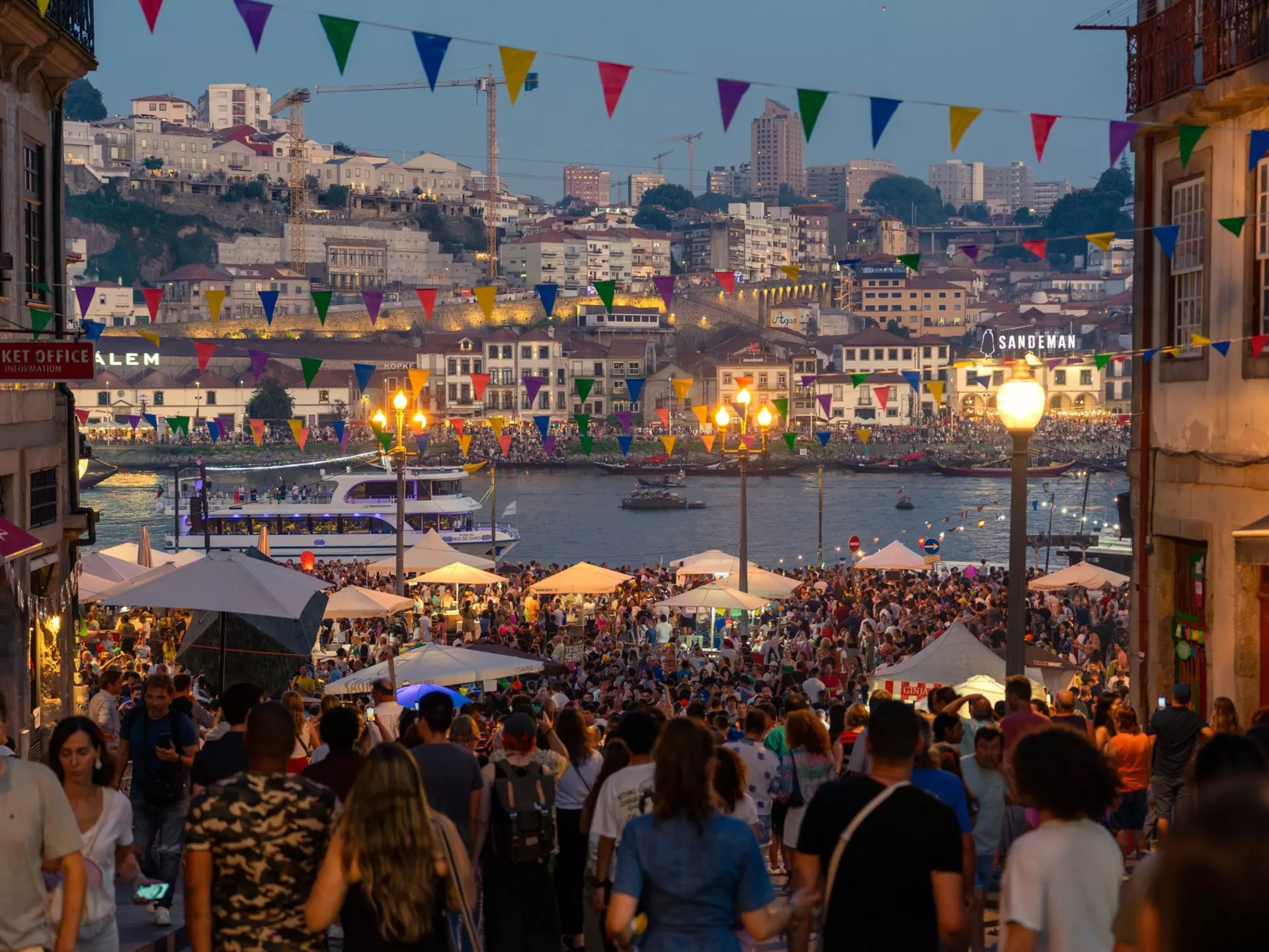 Revellers fill the streets during an evening festival beside a river.