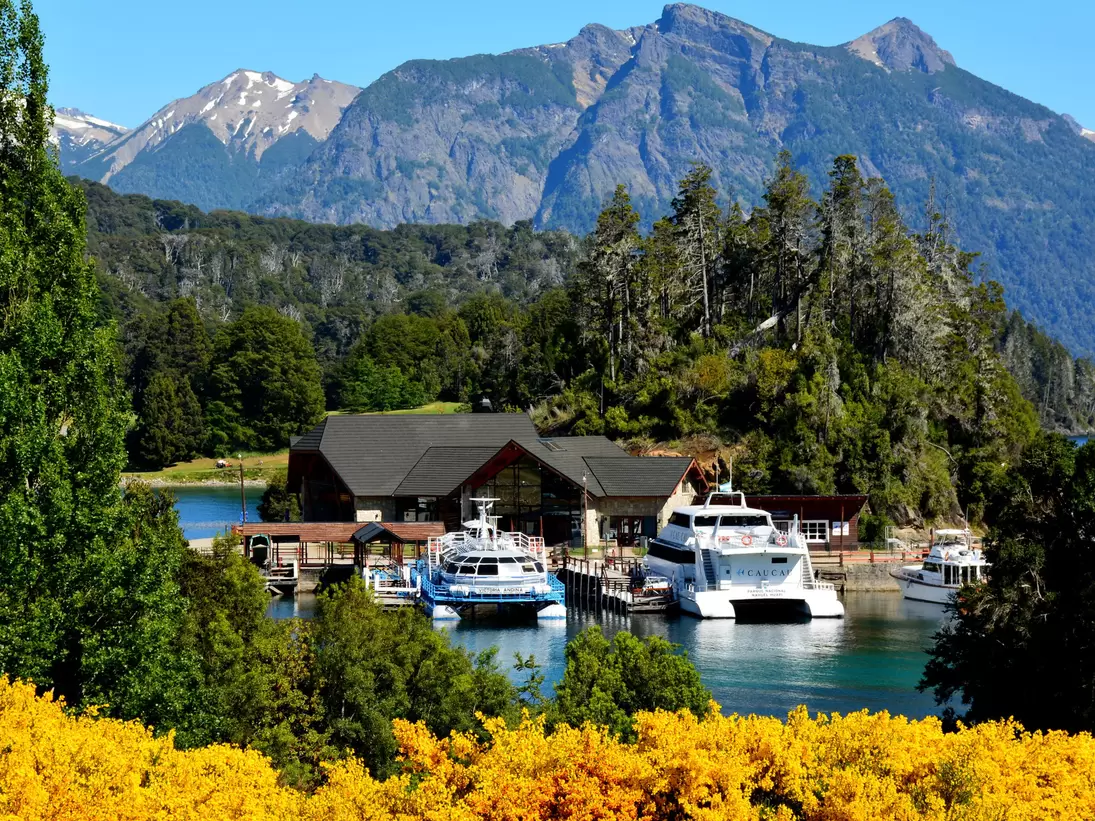 Boats docked at Puerto Pañuelo with trees and mountain range in the background. Bariloche. Rio Negro, Argentina.