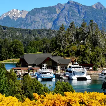 Boats docked at Puerto Pañuelo with trees and mountain range in the background. Bariloche. Rio Negro, Argentina.