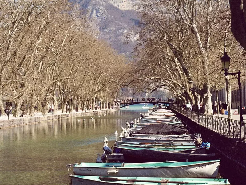 Boats line a long, tree-lined canal leading up to a bridge