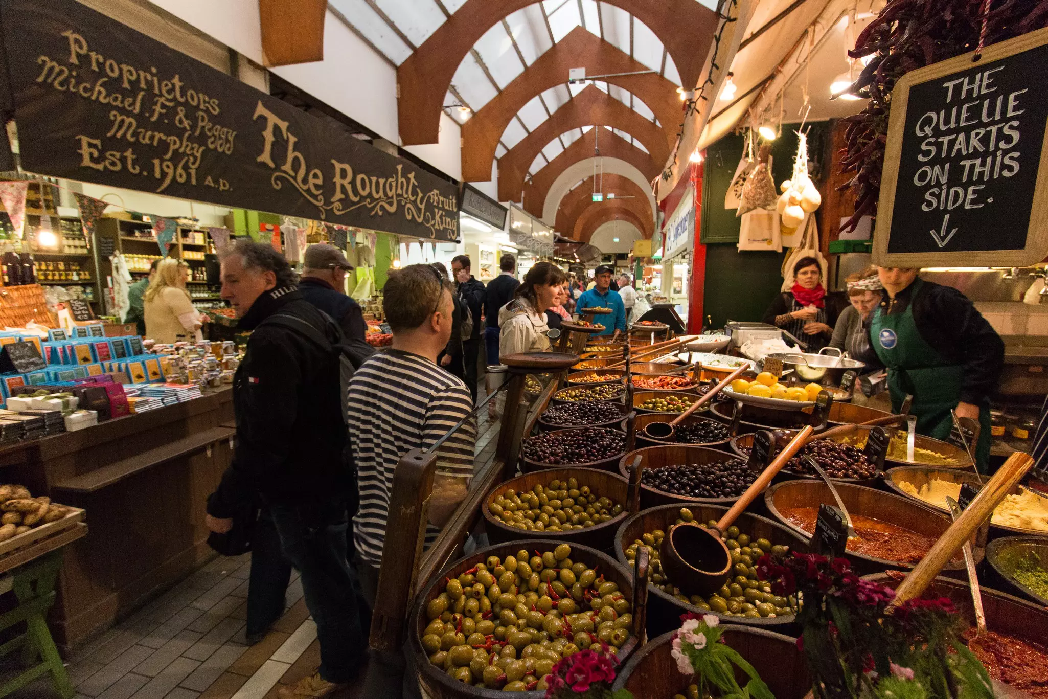 People look at a stand with vats of olives and other food stalls at an indoor market in Cork city, Ireland.