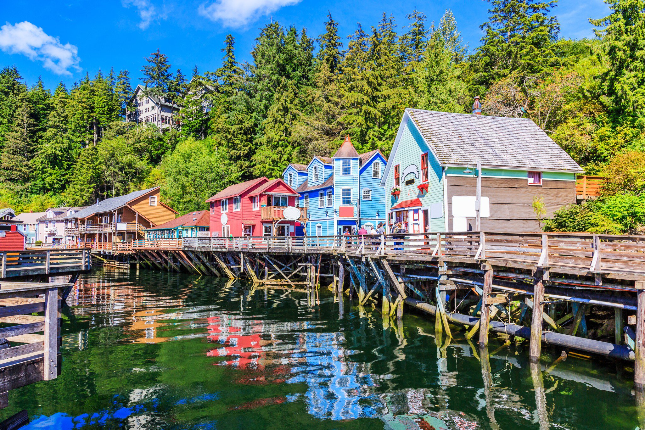 A wooden boardwalk in front of harborfront homes and shops on a sunny day