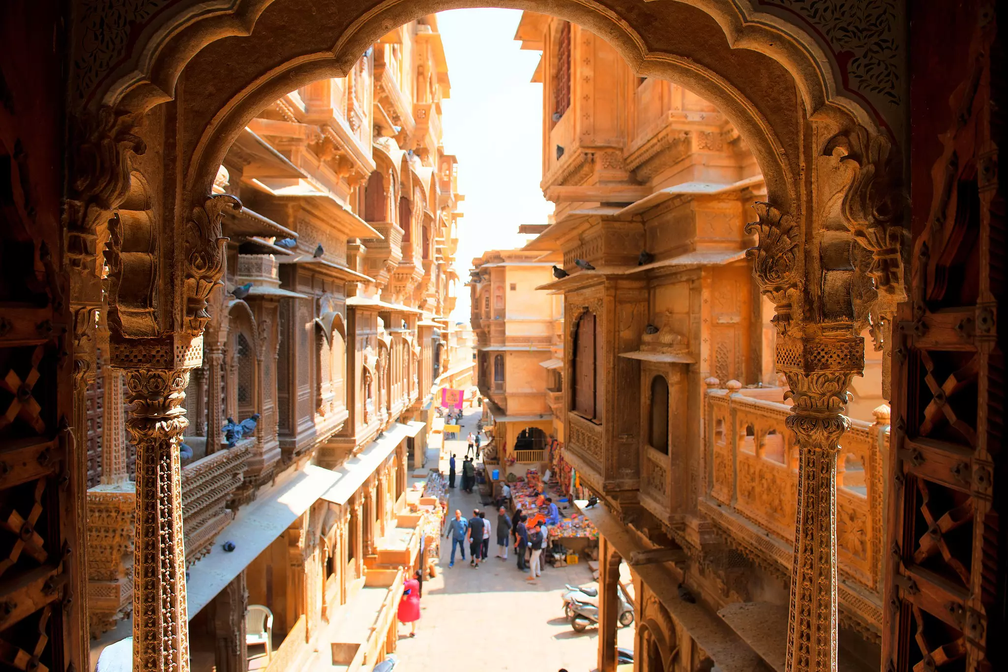 A view of a narrow street showing vendors in buildings with elaborately carved balconies and columns