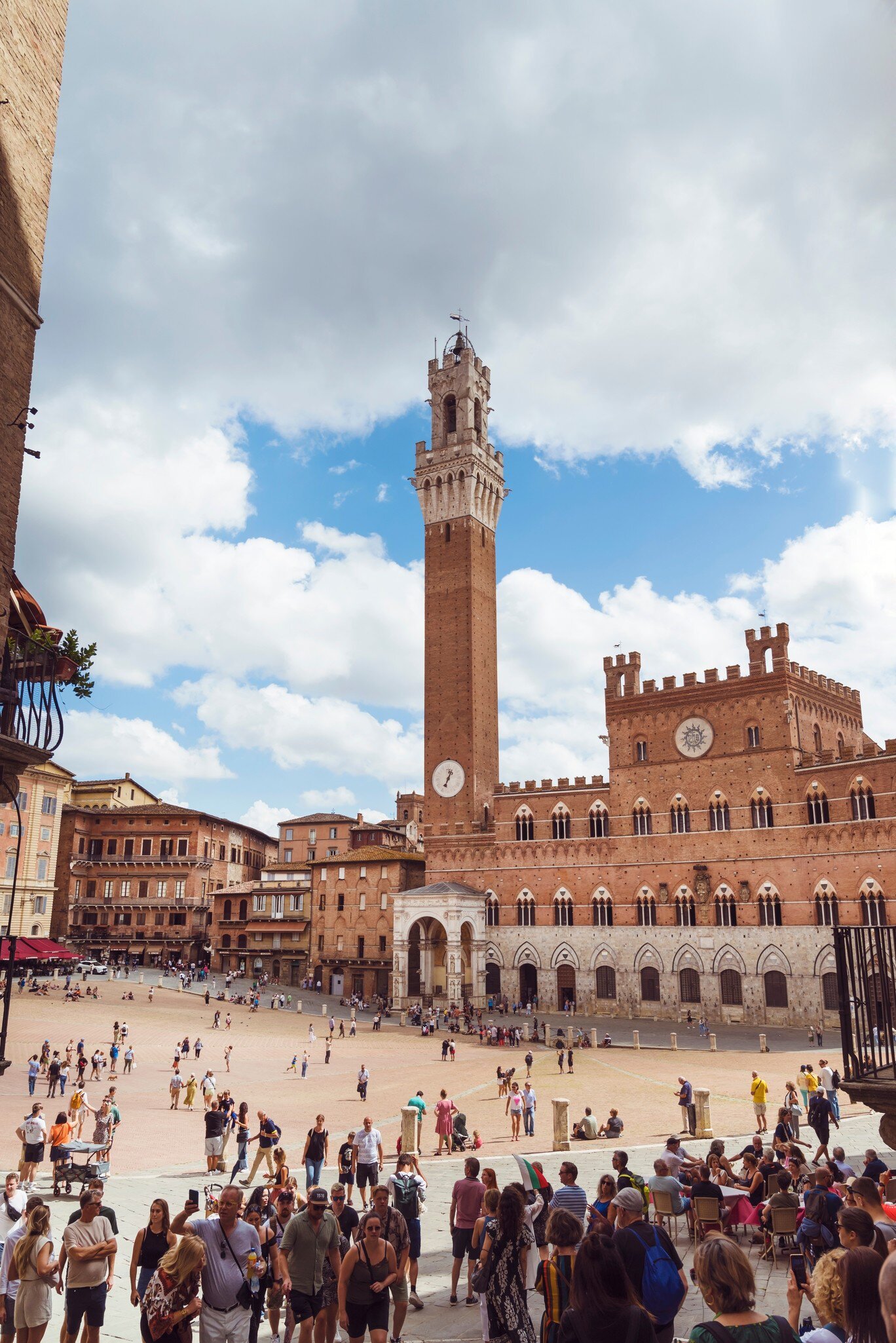 Crowds of people gathered in front of Piazza del Campo and Torre del Mangia on a cloudy day.
