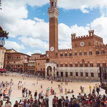 Crowds of people gathered in front of Piazza del Campo and Torre del Mangia on a cloudy day.