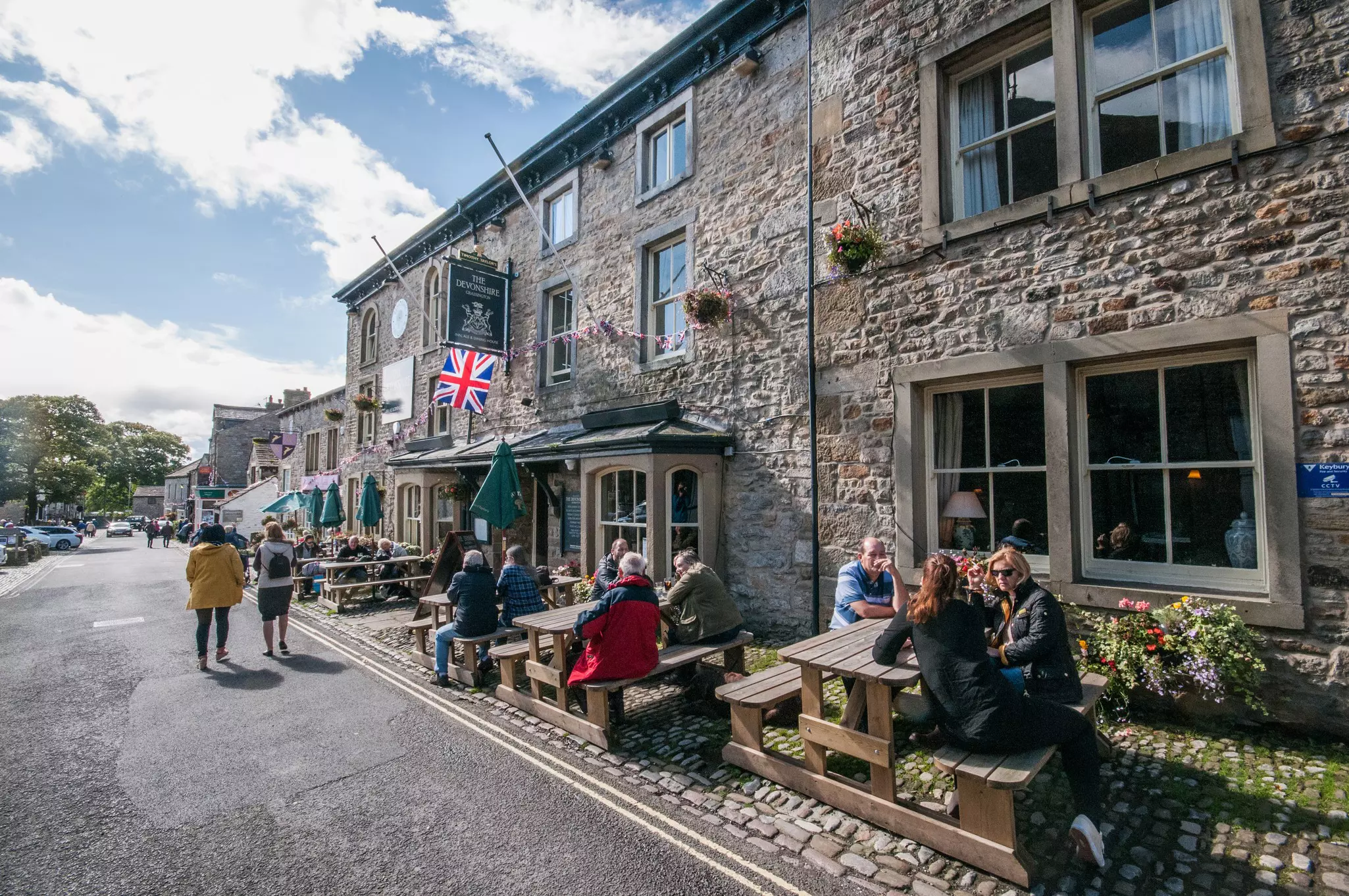 People socializing on a sunny day outside a traditional English pub in Grassington, in Yorkshire Dales National Park, England.