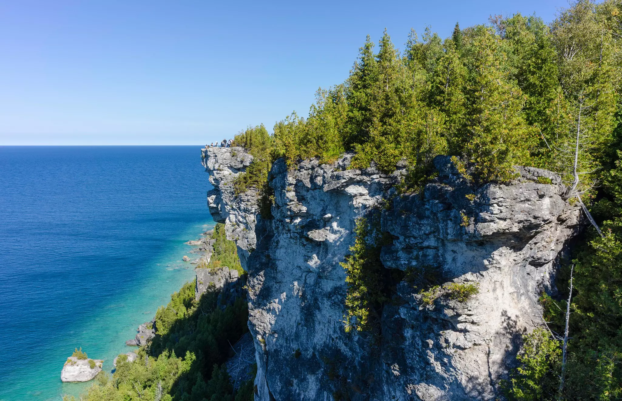 Limestone cliffs in Ontario, Canada, border open water; a narrow strip of water is aqua by the shore, then darker blue beyond.